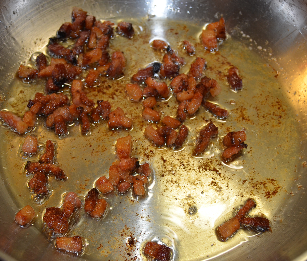 Guanciale pieces frying on a pan.