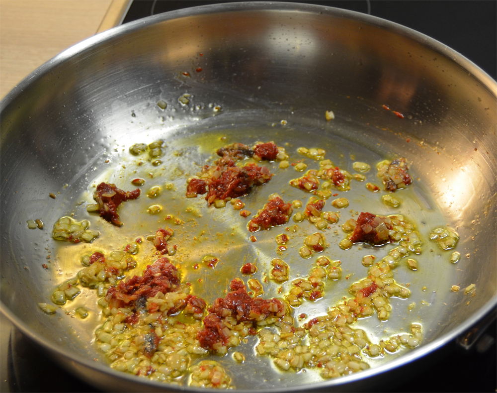 Shallots, anchovy fillets and tomato paste on a skillet.